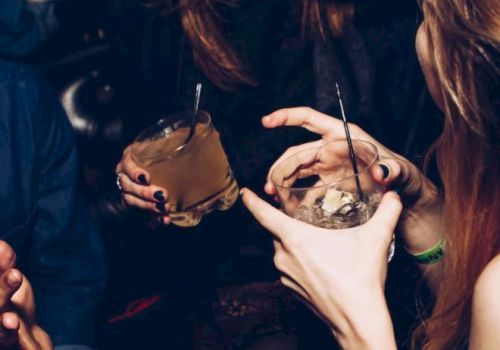 Two people appear to be enjoying drinks in a social setting, laughing and chatting, with close-up views of their hands holding glasses.