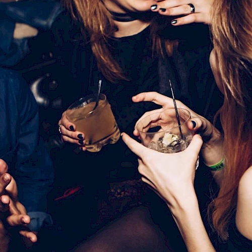 Two people appear to be enjoying drinks in a social setting, laughing and chatting, with close-up views of their hands holding glasses.