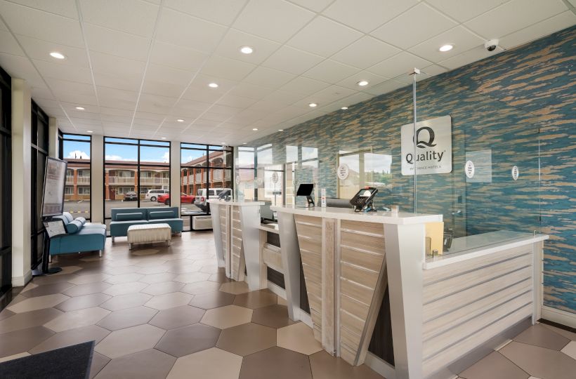 The image shows a modern hotel lobby with a reception desk, seating area, and large windows. The decor includes a blue accent wall and tiled floor.