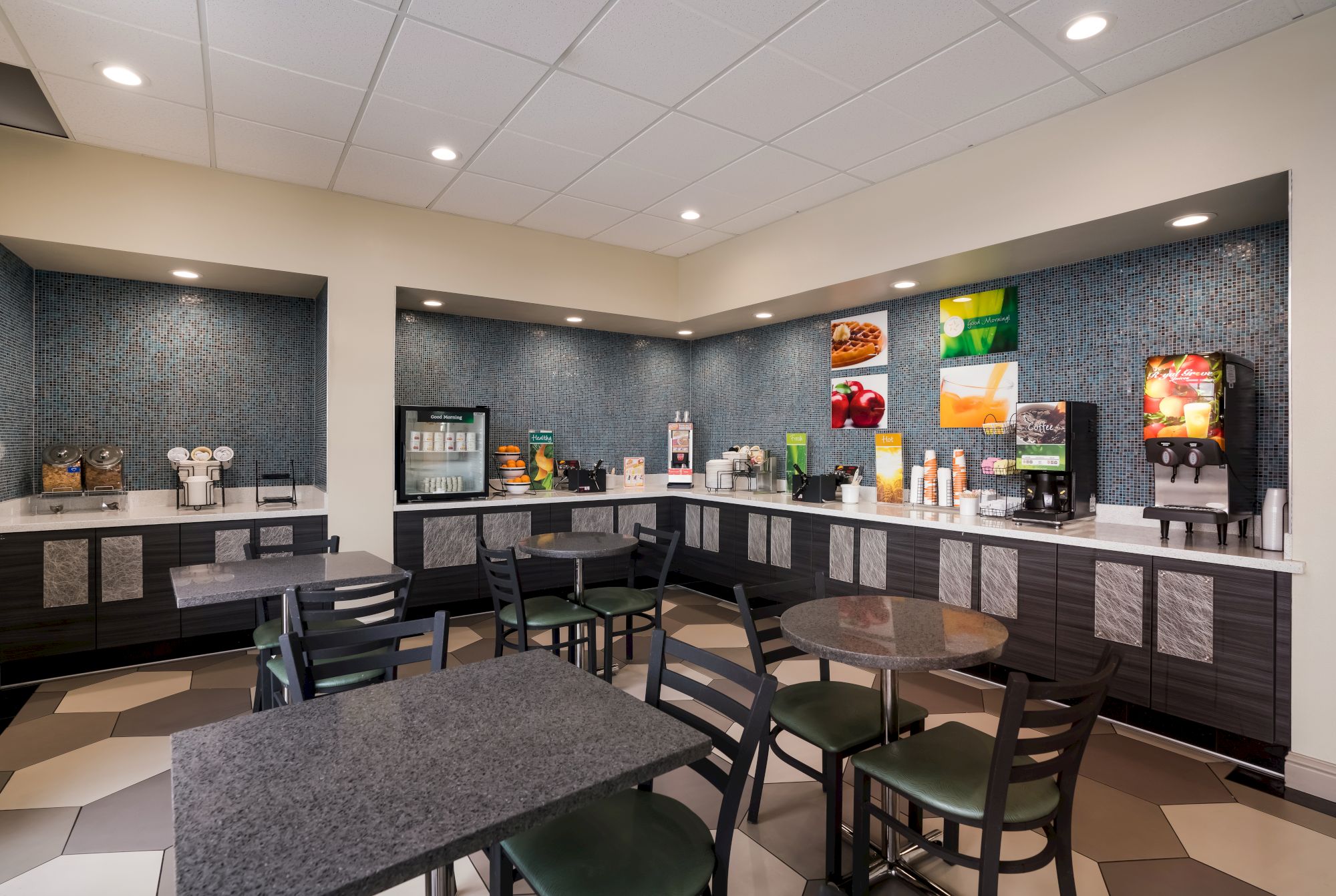 The image shows a modern breakfast area with tables, chairs, a drink dispenser, and a variety of breakfast items and appliances.