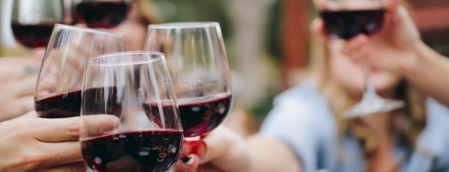 A group of people clinking glasses of red wine in a celebratory toast outdoors, indicating a social gathering or celebration.