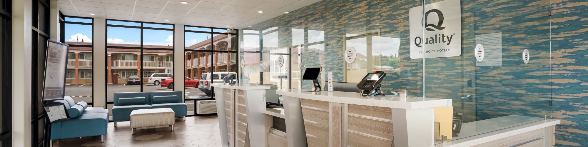 This image shows a hotel lobby with modern decor, a reception desk, seating area, and large windows providing natural light.