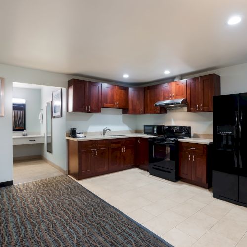 A kitchen with dark wooden cabinets, black appliances including a fridge and stove, and a connected area leading to a tiled bathroom space ending the sentence.