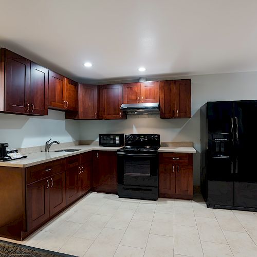 This image shows a modern kitchen with dark wood cabinets, a black refrigerator, a black oven, a microwave, and countertop appliances.