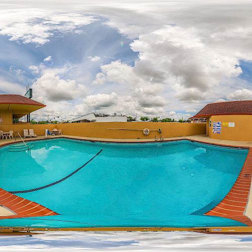 An outdoor swimming pool with several white lounge chairs around it, under a partly cloudy sky.