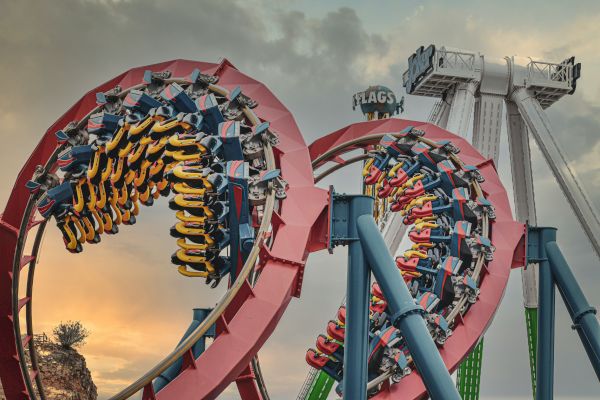 The image depicts a roller coaster with loops and another ride in the background, creating a thrilling amusement park setting at sunset.