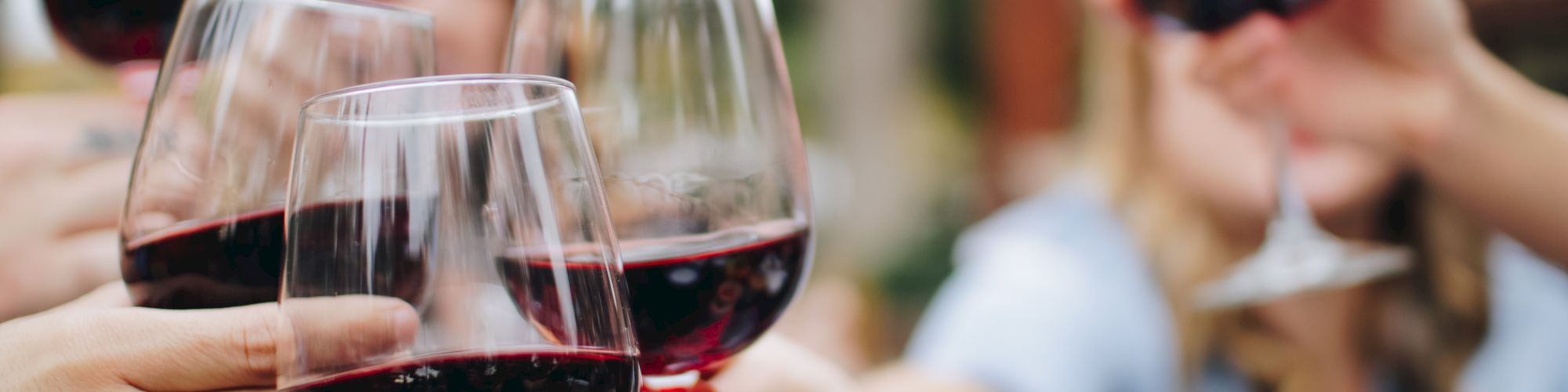 A group of people are raising glasses of red wine in a toast, with blurred background and a focus on the wine glasses.